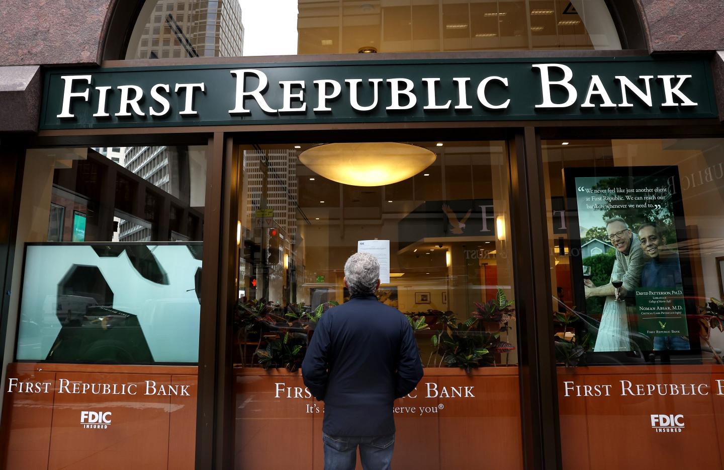 A view of a man wearing a black jacket as he looks up at a First Republic Bank sign