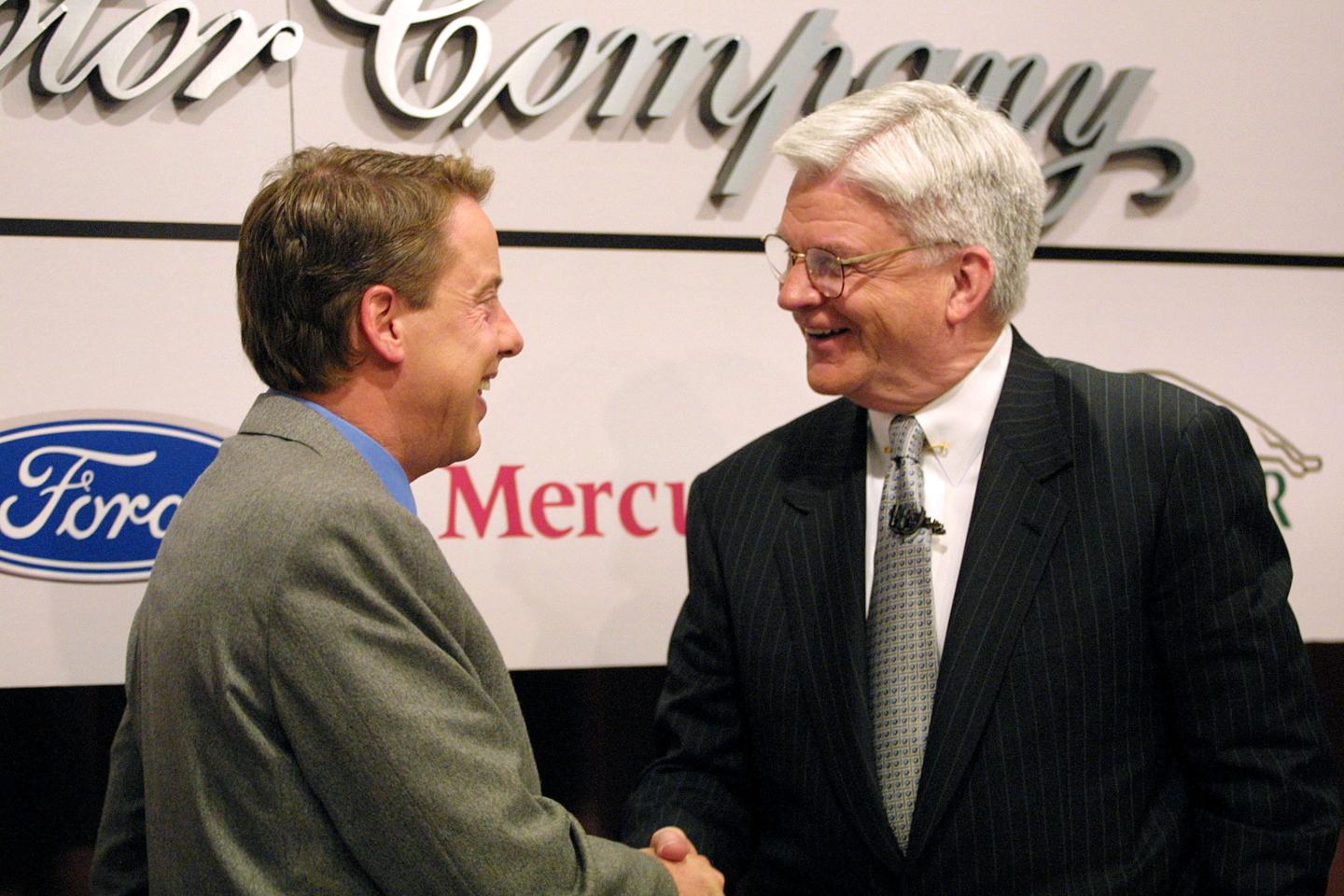 Two men shake hands with the Ford logo behind them