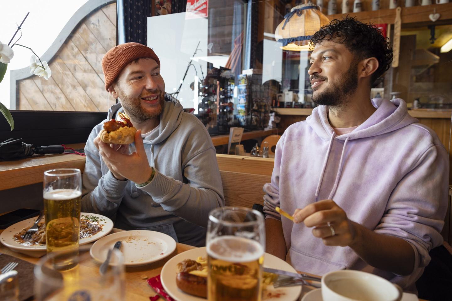 Two men sit at a restaurant booth chatting with food in front of them.