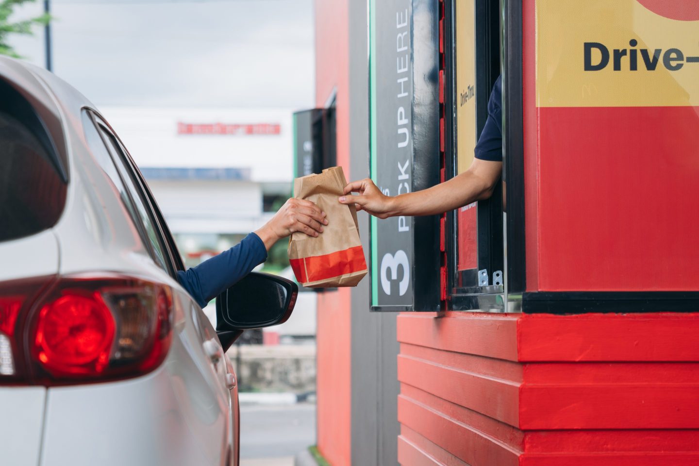 oung Man receiving a bag of food at drive thru counter.