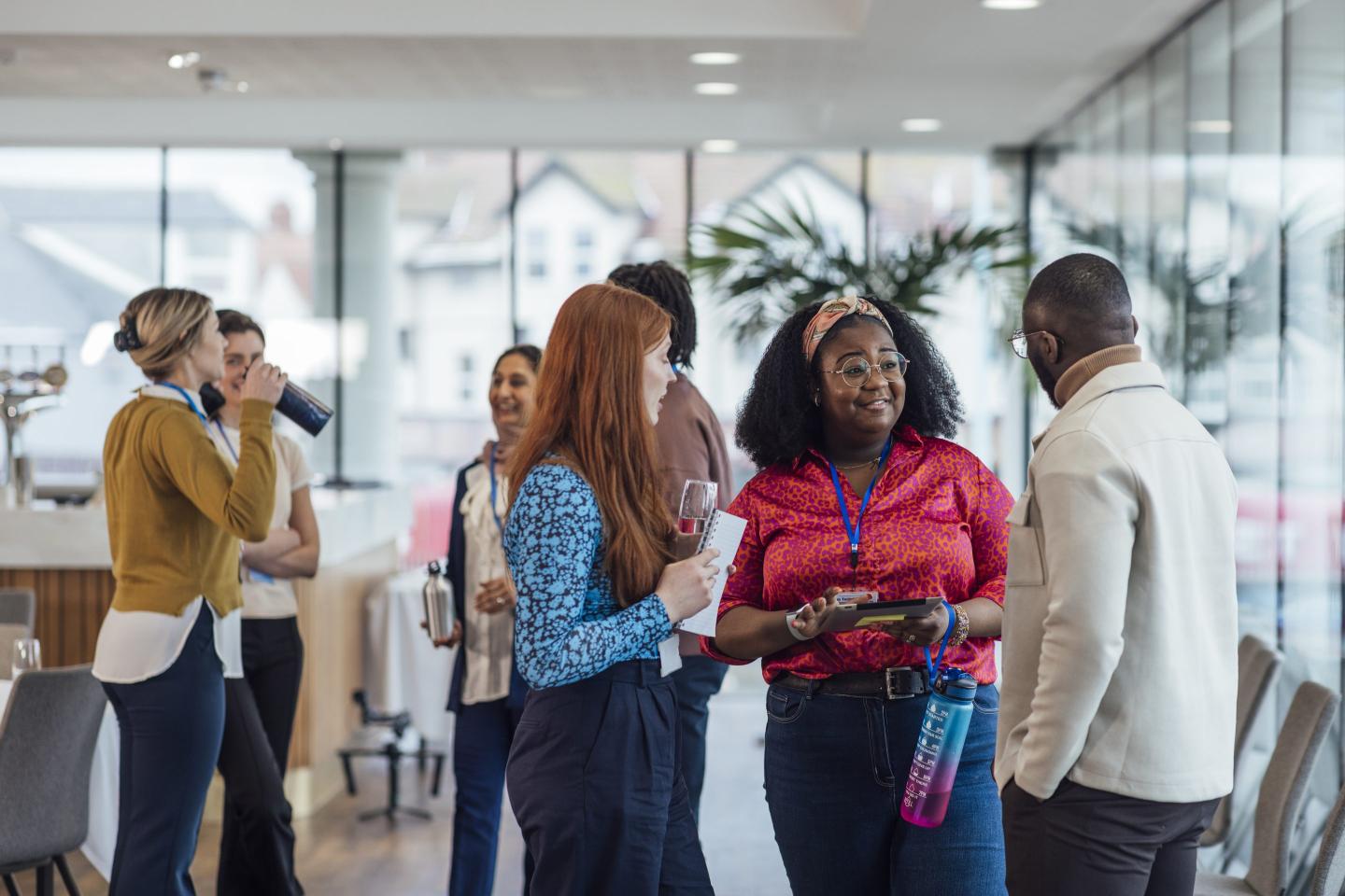 A group of people dressed in business casual attire stand and converse in a meeting room.