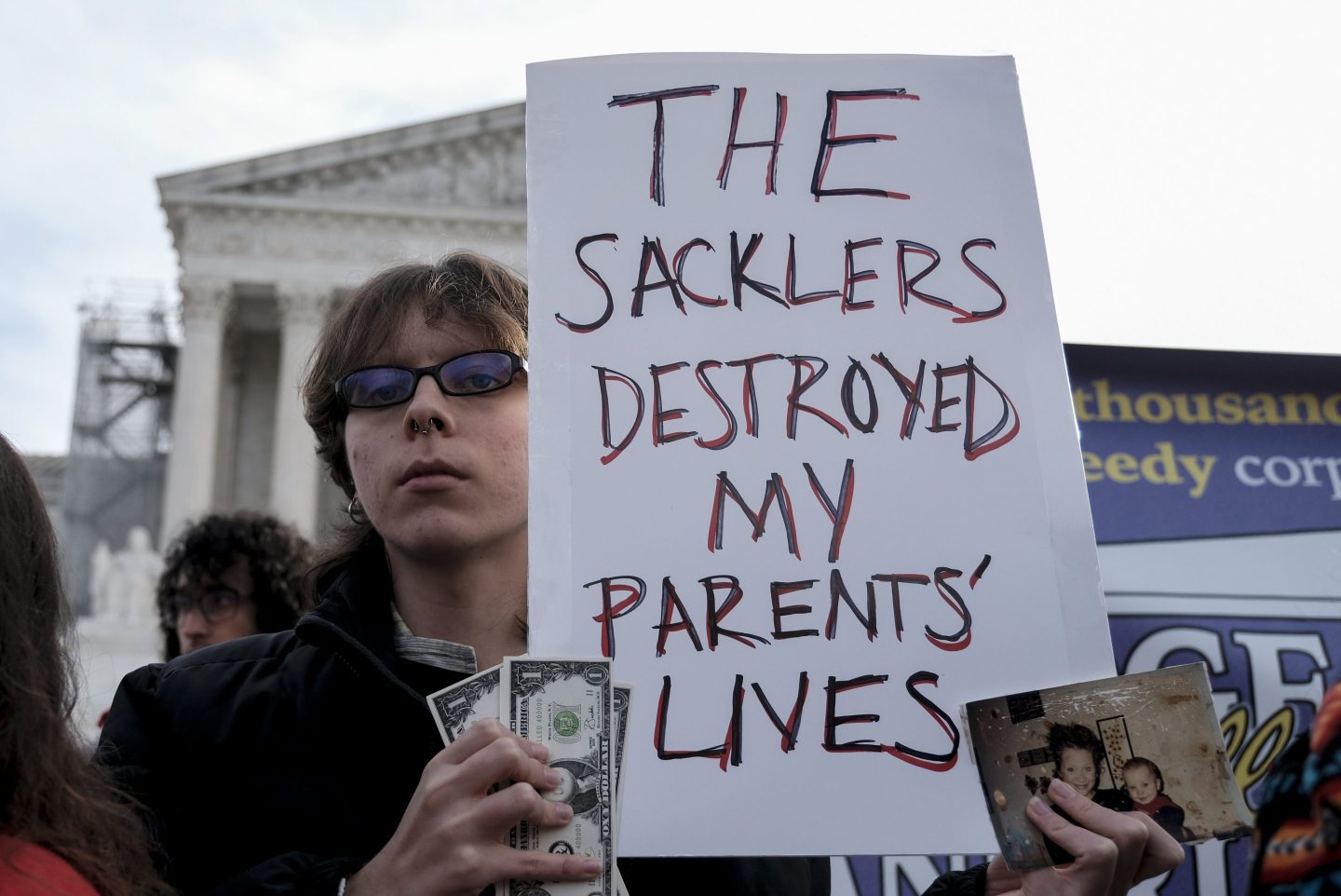 A person stands outside of the Supreme Court holding a sign which reads "The Sacklers destroyed my parent's lives."