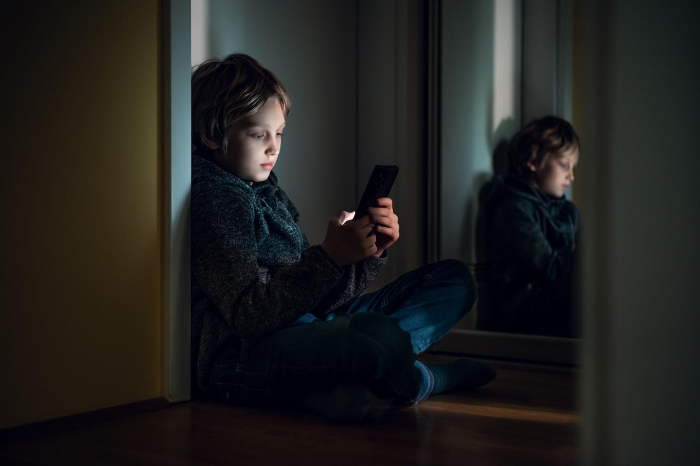 young boy sitting in the dark on his smartphone