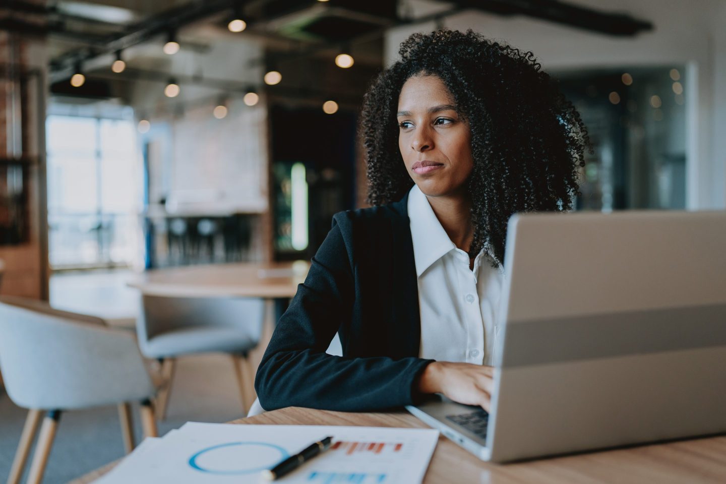 Young businesswoman using laptop at table looking to side.