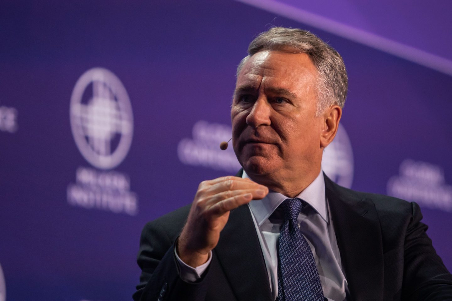 Ken Griffin mid-word with his hand raised in front of a purple background.