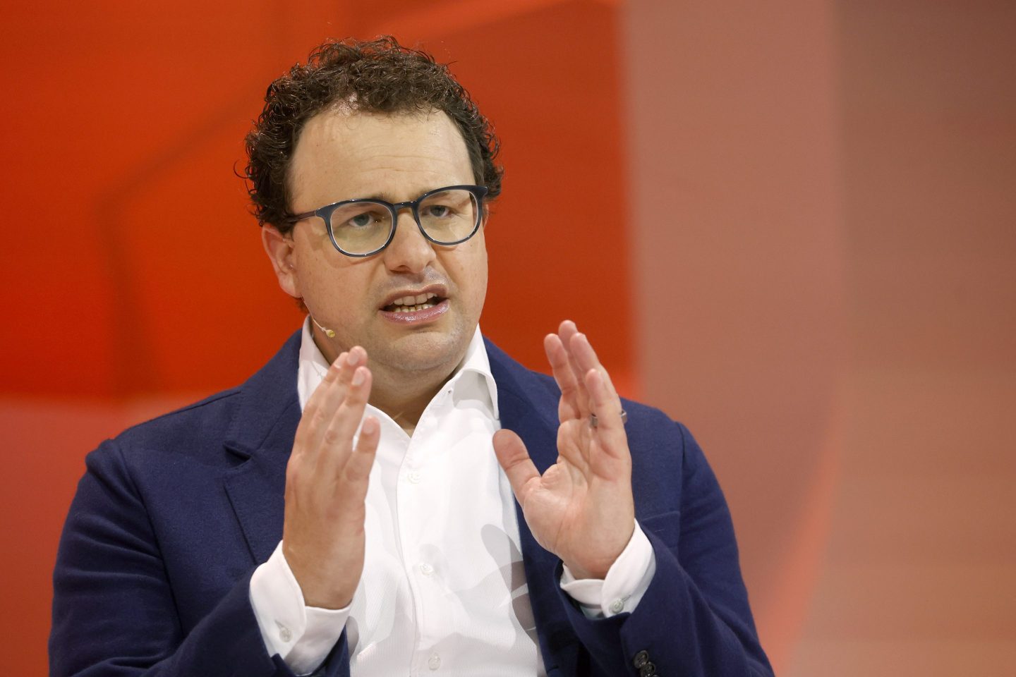 Anthropic cofounder and CEO Dario Amodei wearing a white shirt and blue jacket, photographed against a red backdrop, gesturing with his hands while on stage.