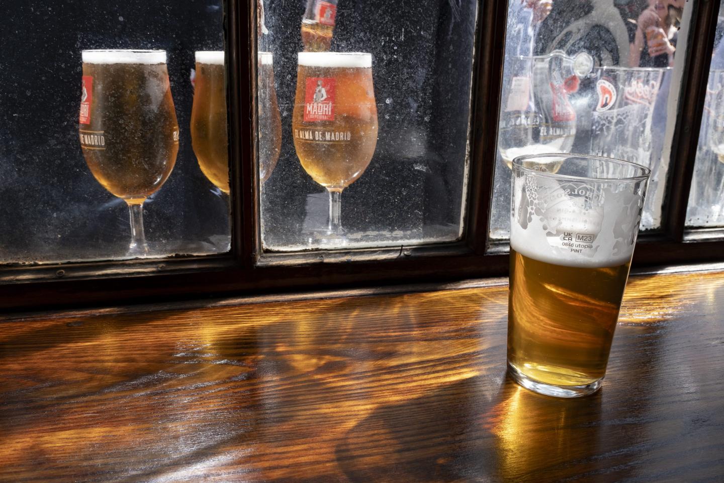 Pint of English ale on a pub table and pints of Madri lager seen through the pub window on 9th May 2024 in London, United Kingdom.