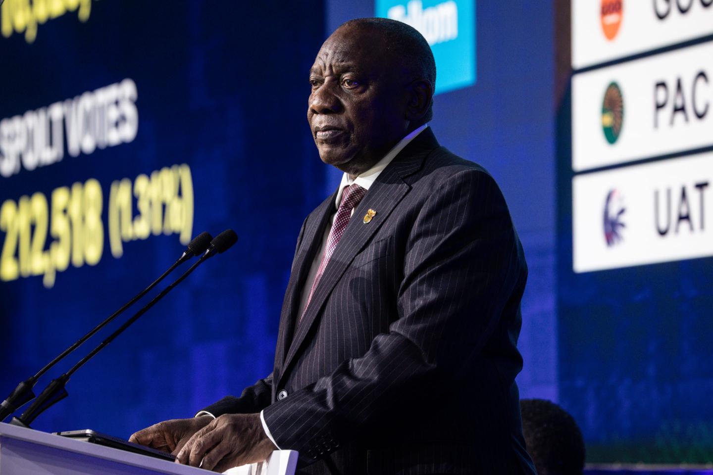 South African President Cyril Ramaphosa stands in a suit behind a podium, frowning.