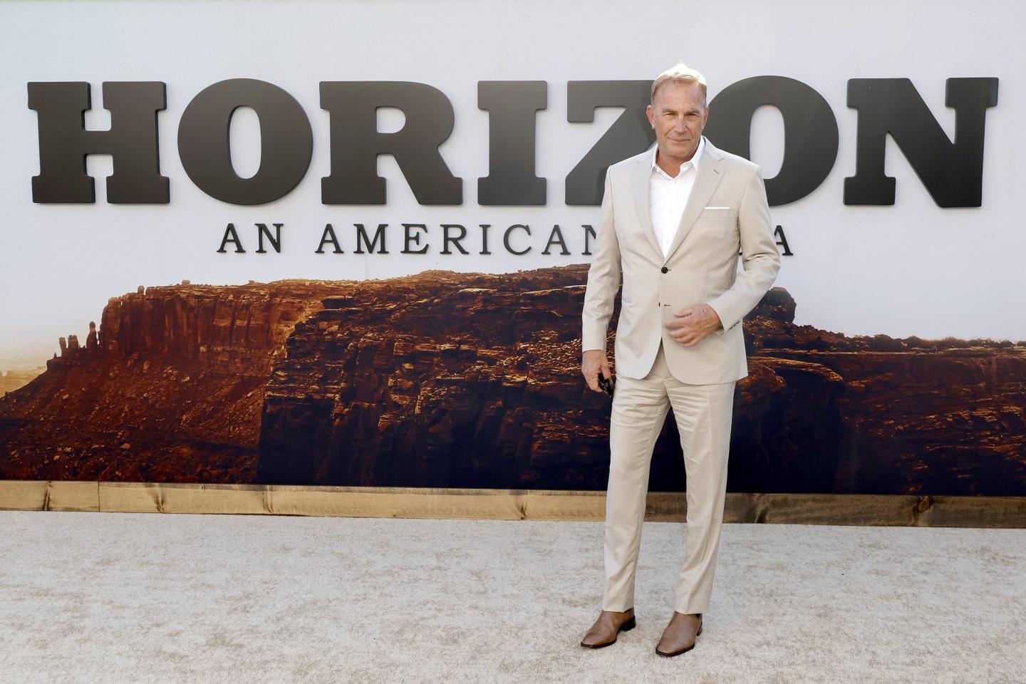 Kevin Costner stands in front of poster