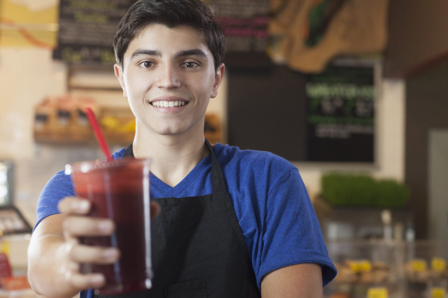 A young man in an apron holds a cold drink out and smiles