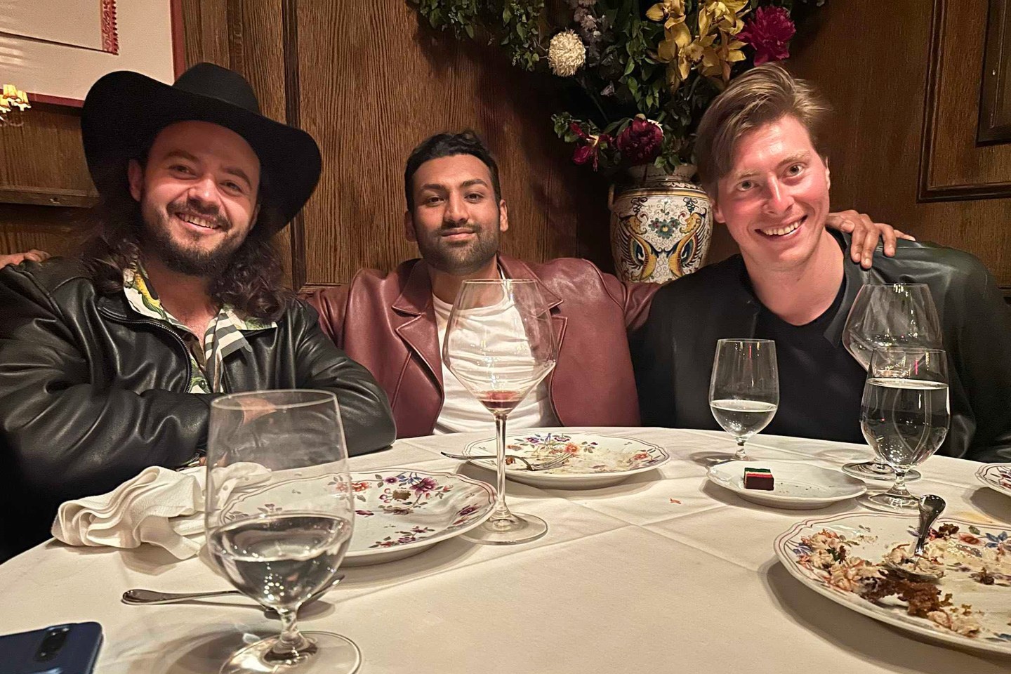 three men lean towards one another for a photo while sitting at a dinner table