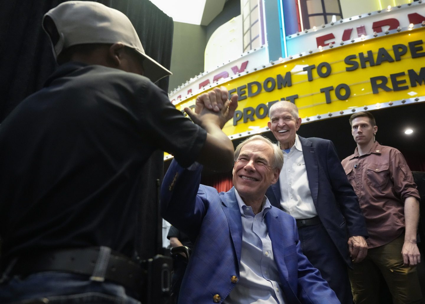 A kid, left, high-fives Gov. Greg Abbott after a press conference on Hurricane Beryl as Gallery Furniture Owner Jim "Mattress Mack" Mcingvale, second from right, smiles on July 14, 2024, at Gallery Furniture in Houston.