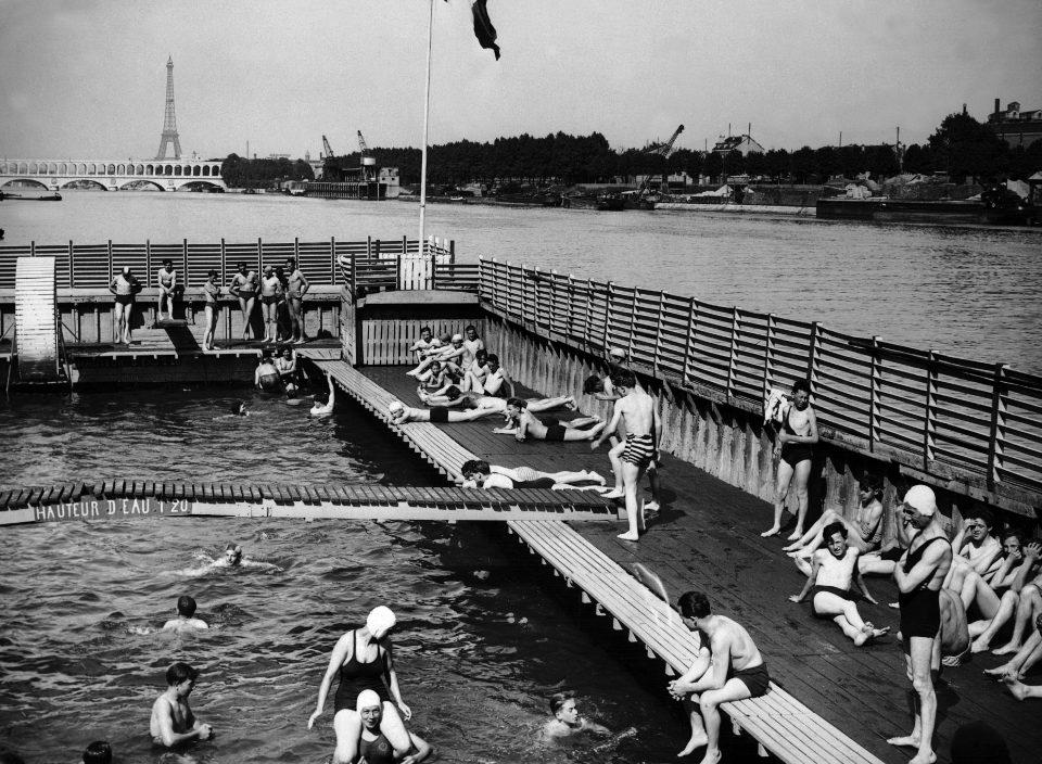 People sitting around and swimming inside a water body, the Seine river 