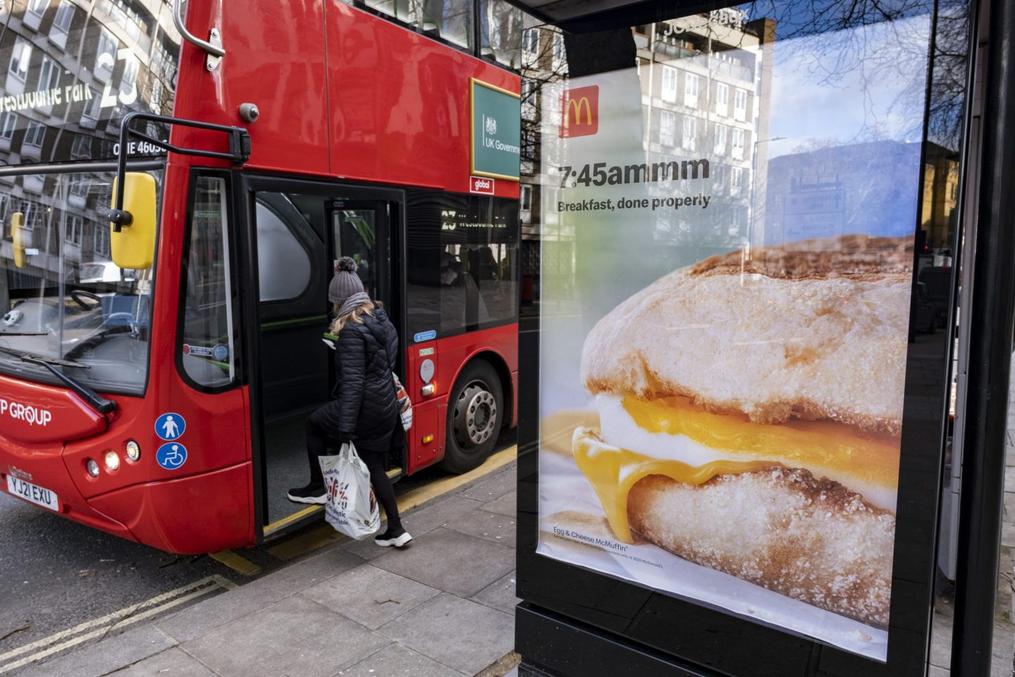 A bus stop with a McDonald's breakfast ad as a passenger walks onto a bus.
