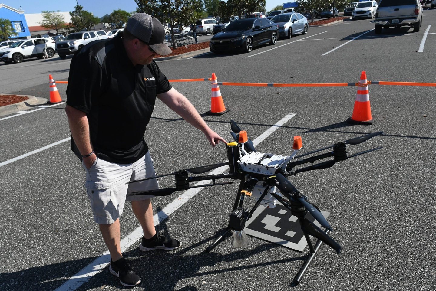 A man stands next to a drone in a parking lot.