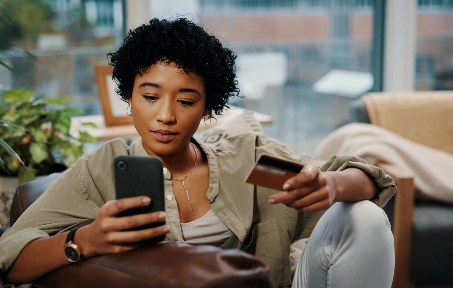 Woman looks at mobile phone while holding credit card
