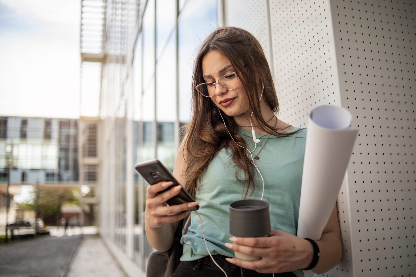 Female student carrying portfolio and coffee while on her phone