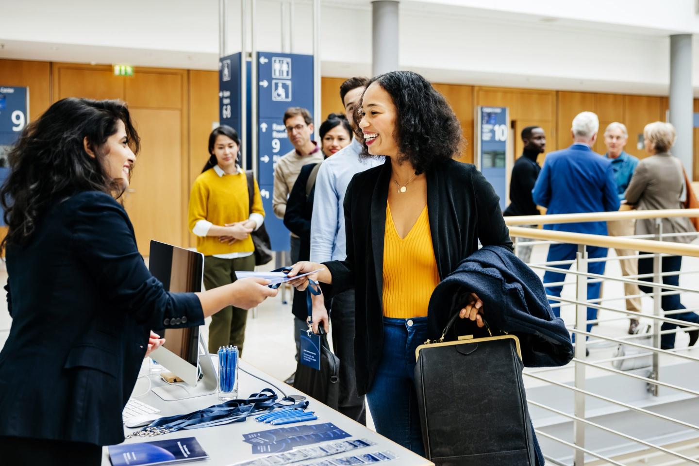 A receptionist giving a participant id to an attendee at a business conference sign in desk.