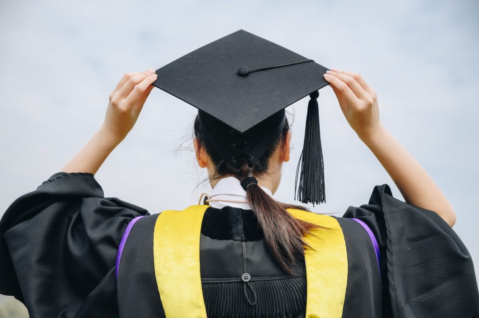Rear view of young student wearing graduation gown and cap