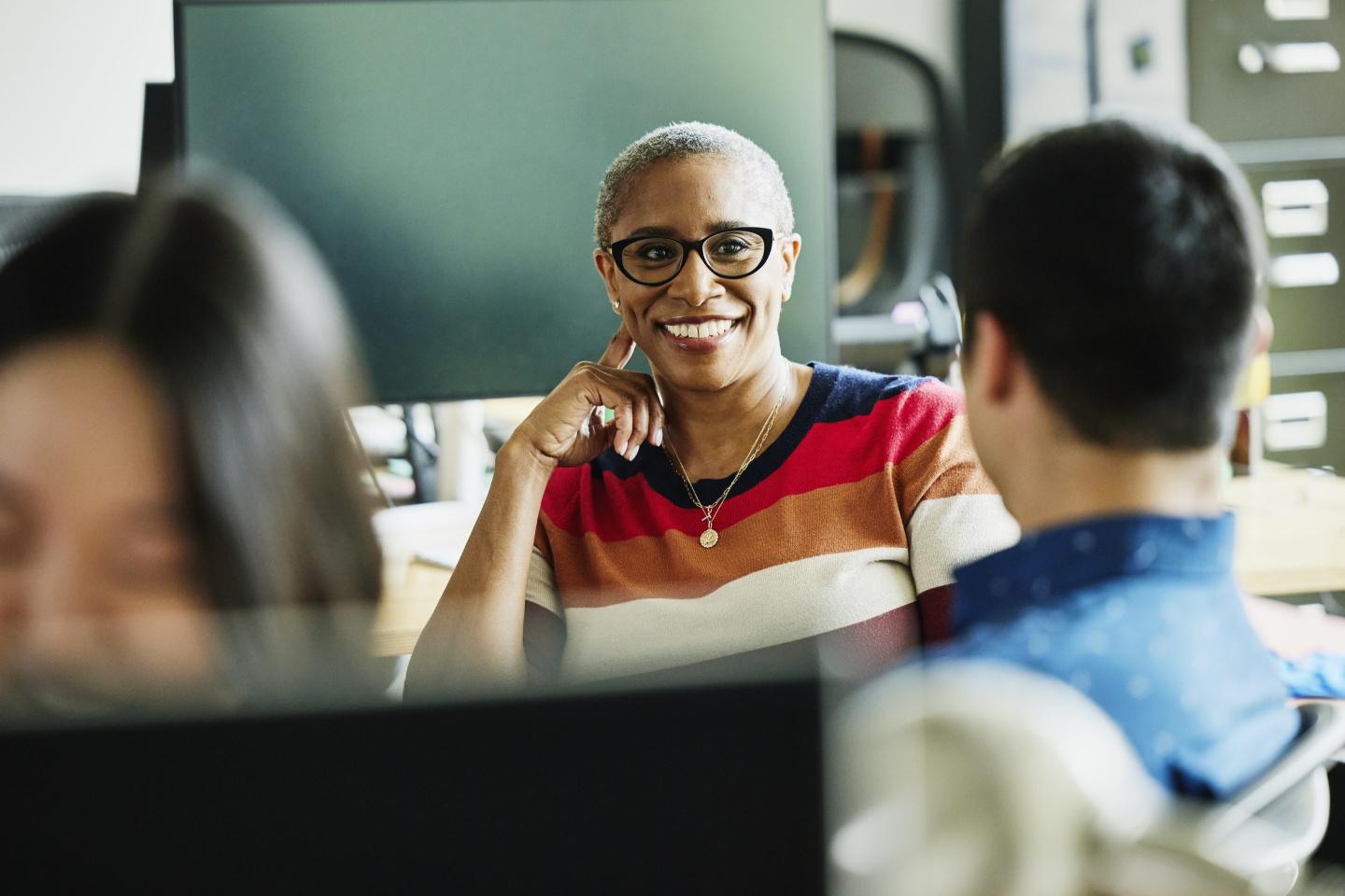 Medium shot of smiling mature businesswoman in discussion with colleagues at workstation in creative office