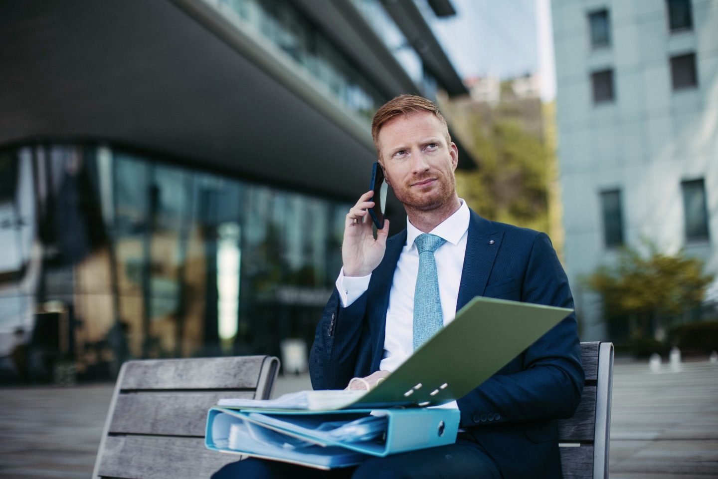 Serious businessman reading document from file folder while calling with client.