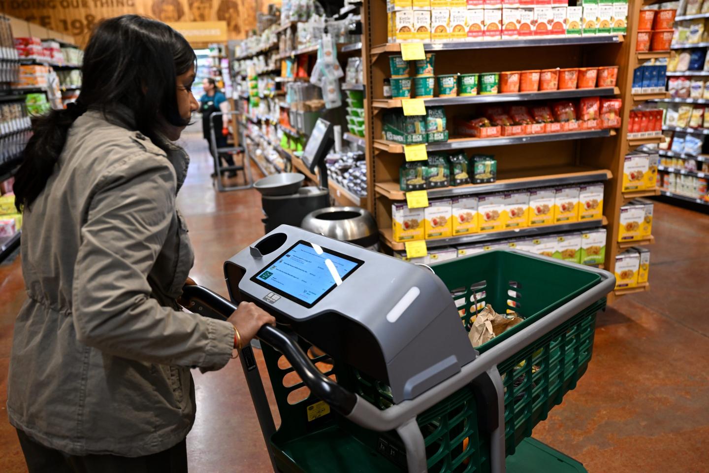 A woman pushes a shopping cart with a screen built into it.