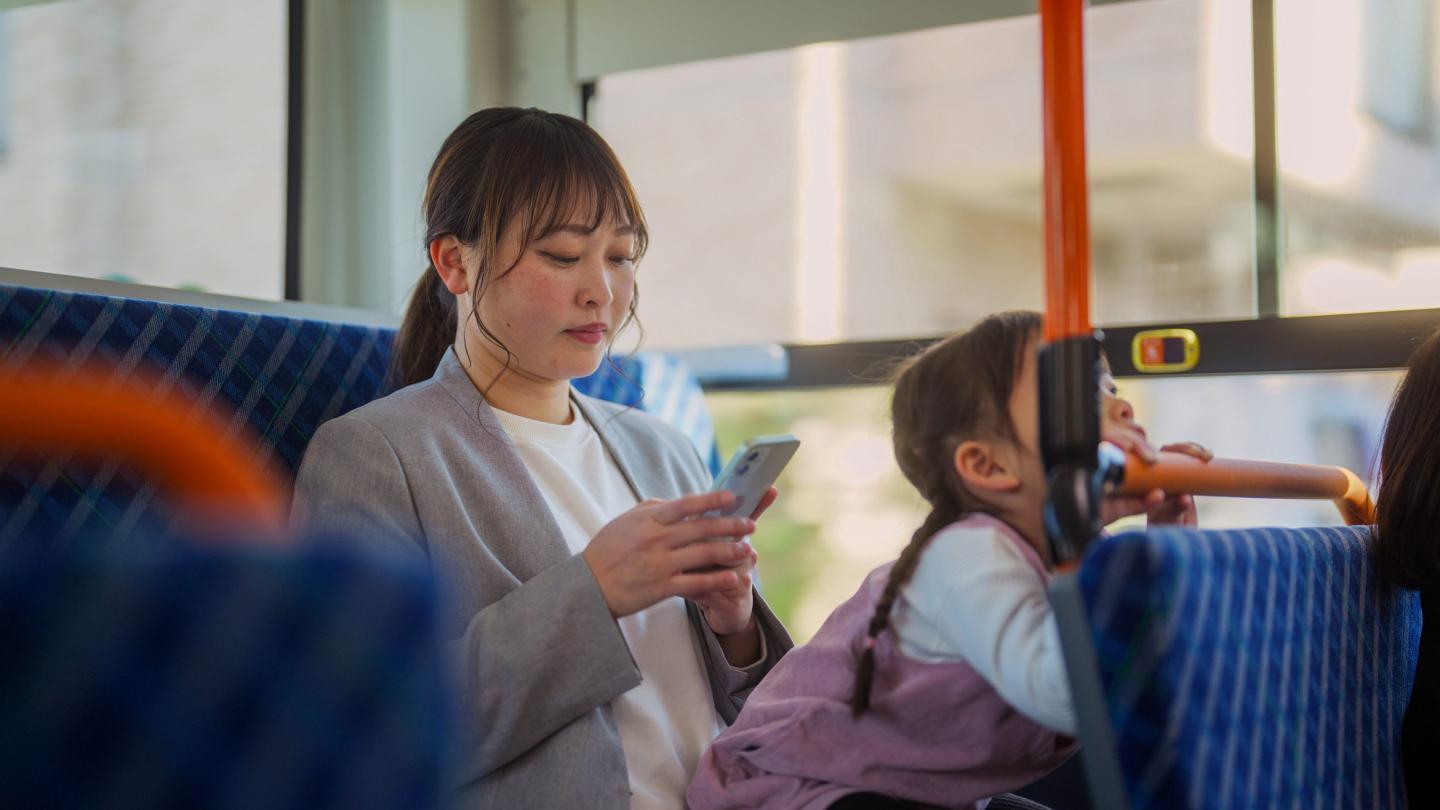 An Asian businesswoman is commuting by bus with her small daughter.