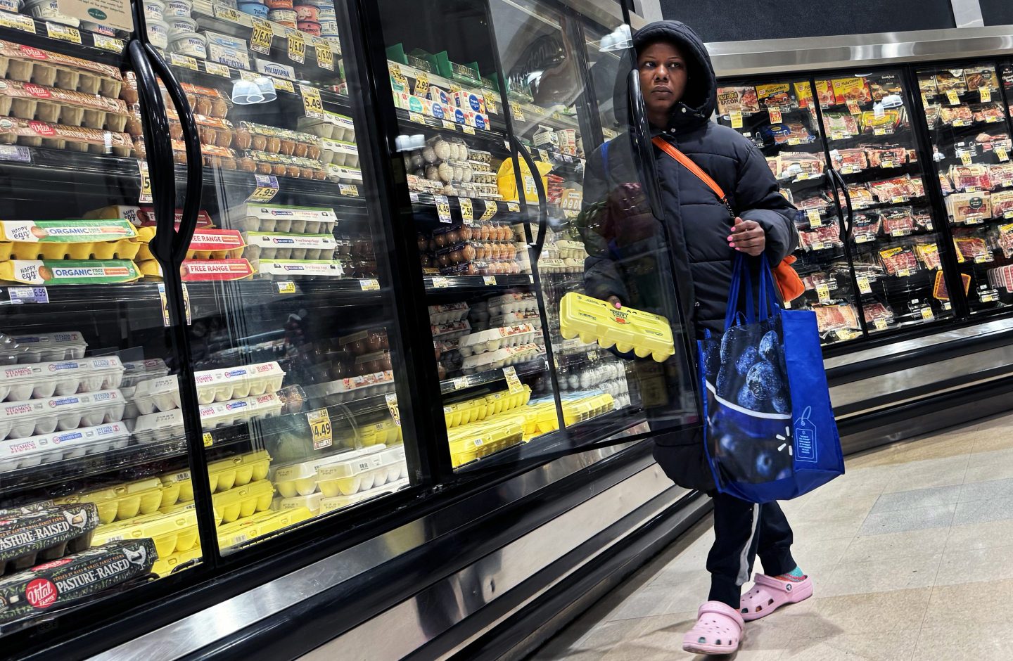 A woman takes a carton of eggs from a refrigerated shelf.