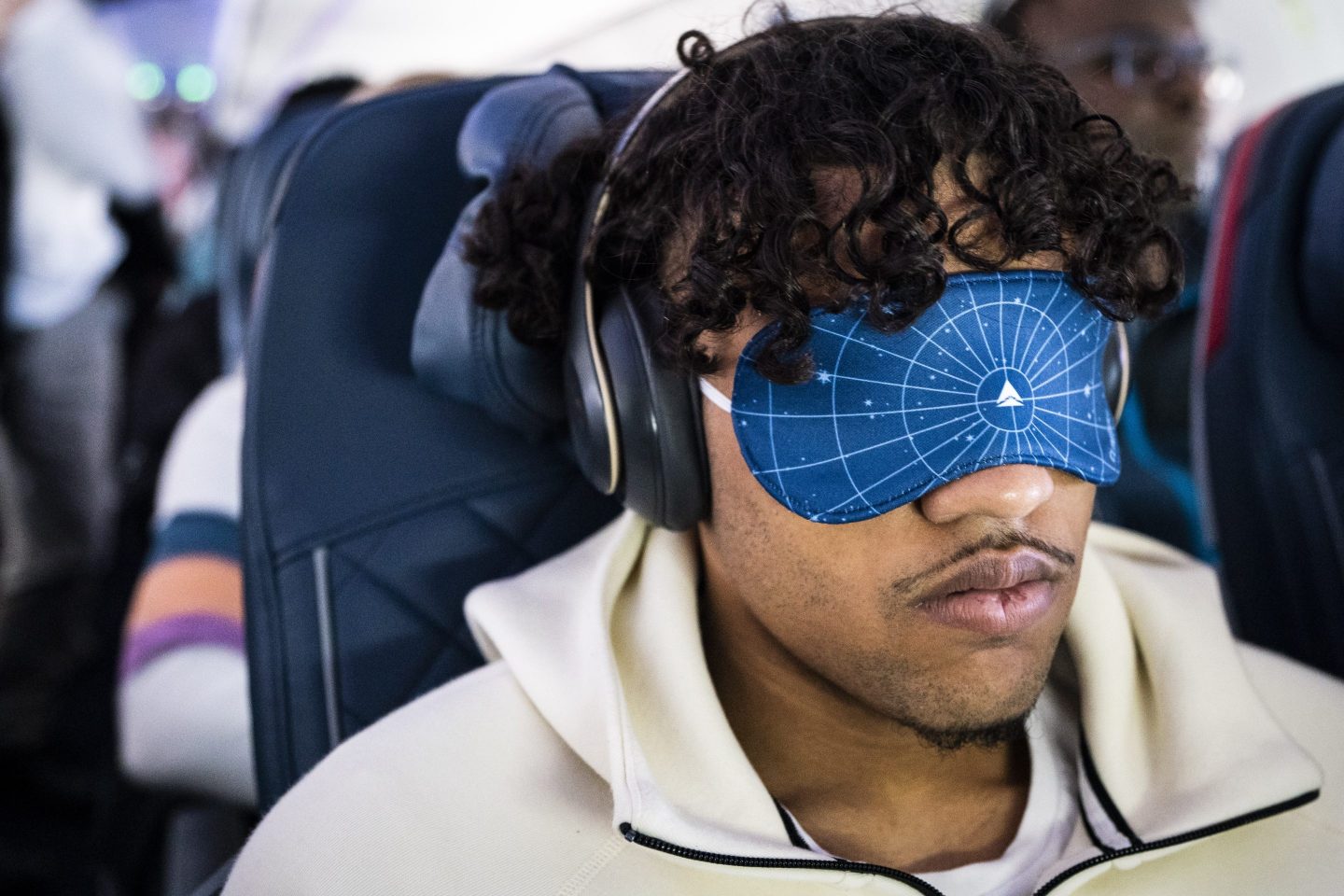 A man sits in a plane seat with an eye mask on.