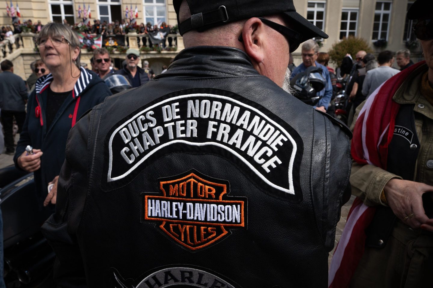 A biker wears a Harley Davidson leather jacket that reads "Ducs de Normandie Chapter France"