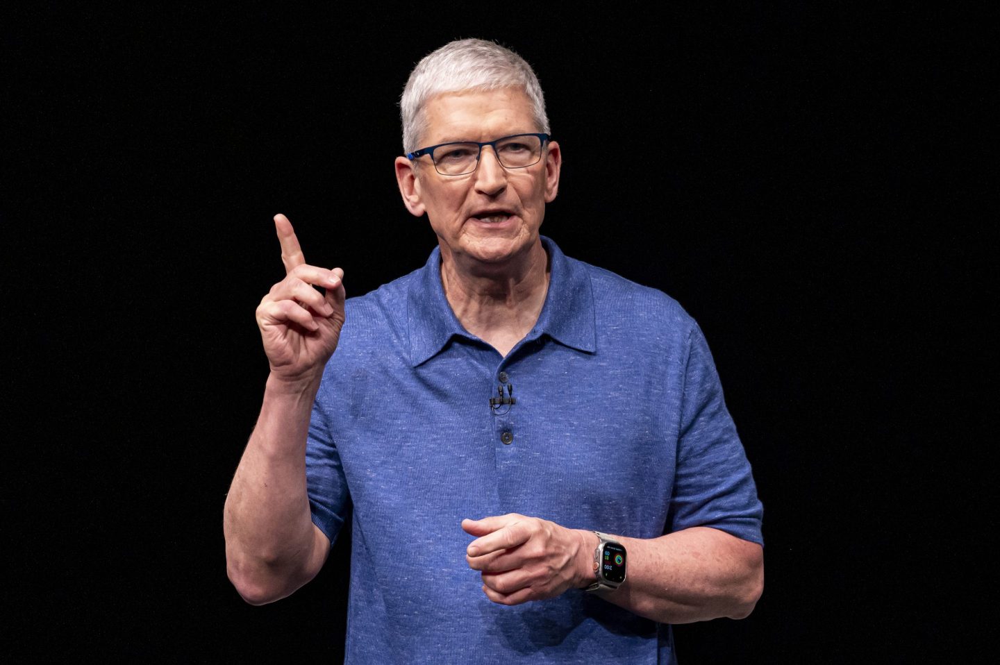 Apple CEO Tim Cook speaks on stage, his right index finger raised in the air
