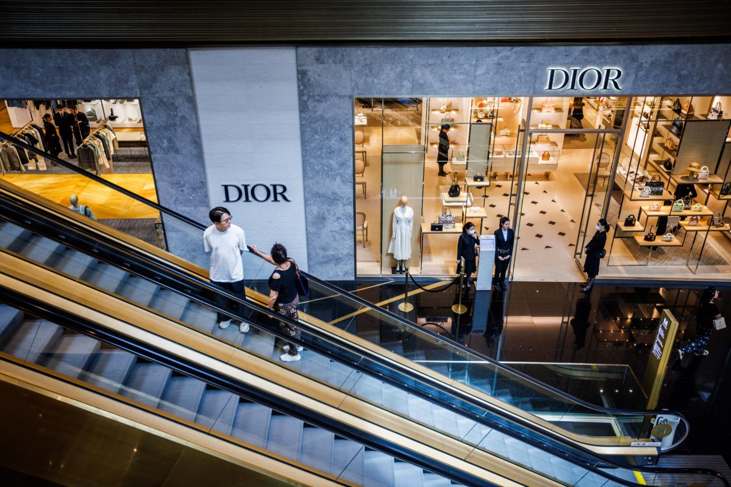 people taking the escalator in front of a Dior store in a mall
