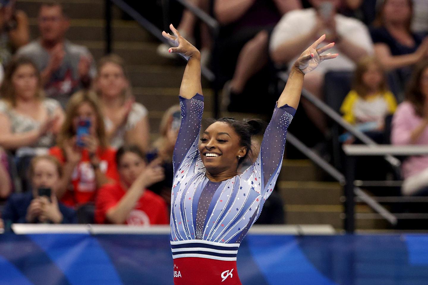 Simone Biles is smiling and lifting her arms in the air.
