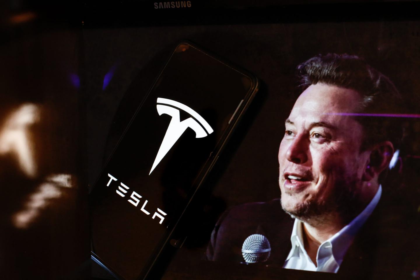 the Tesla logo is seen displayed on a smartphone screen and a computer screen displaying a portrait of Elon Musk