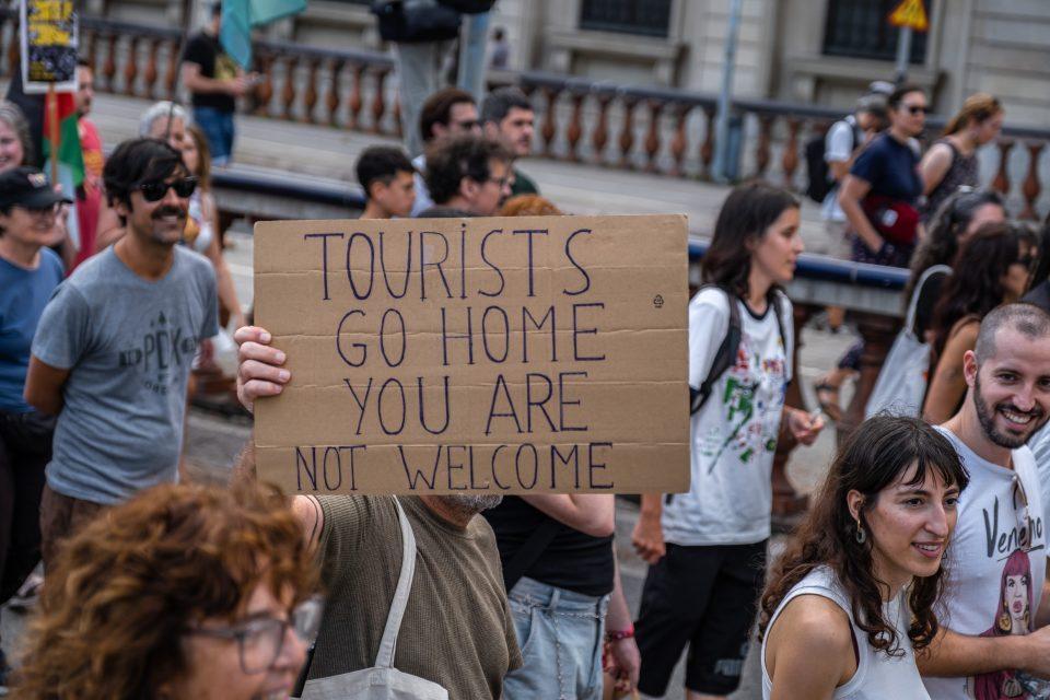 protestors on a street holding an anti-tourism placard 