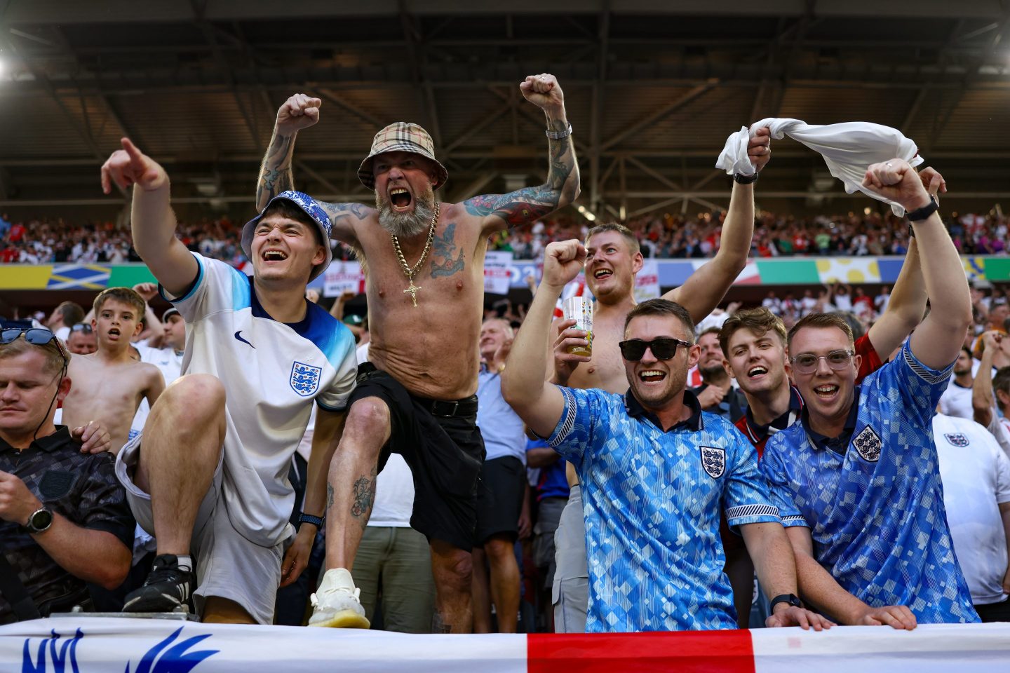 A group of fans in blue and white shirts cheer with their arms in the air.