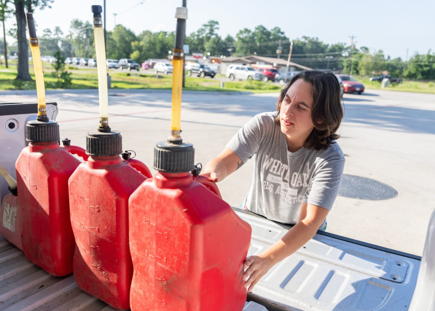 A woman loads containers of gasoline into her truck bed.
