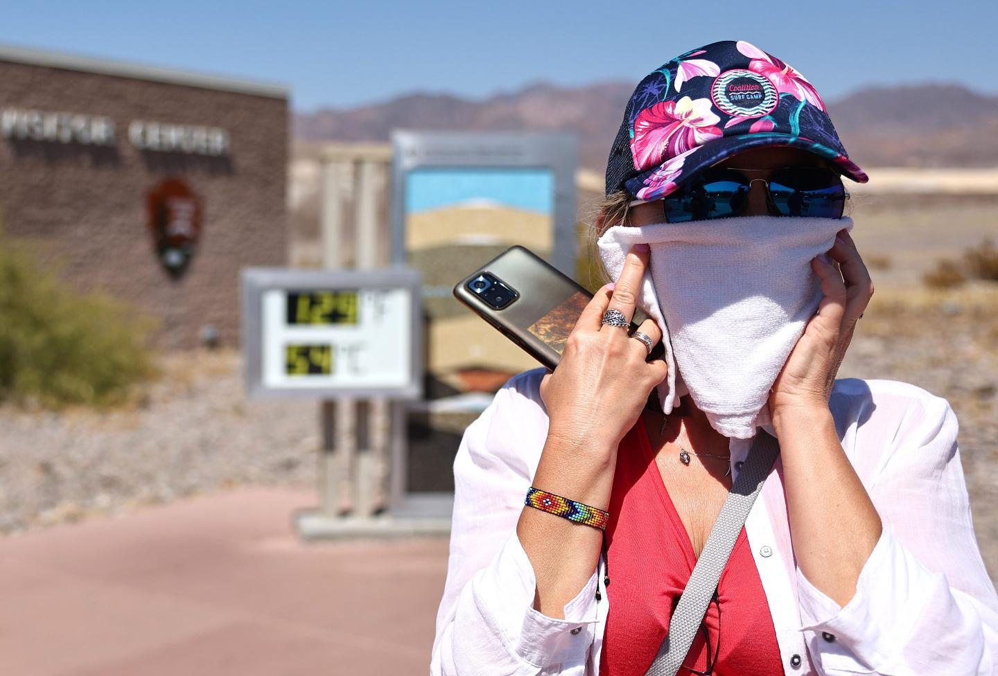 A visitor covers their face with a towel near an unofficial thermometer at Furnace Creek Visitor Center