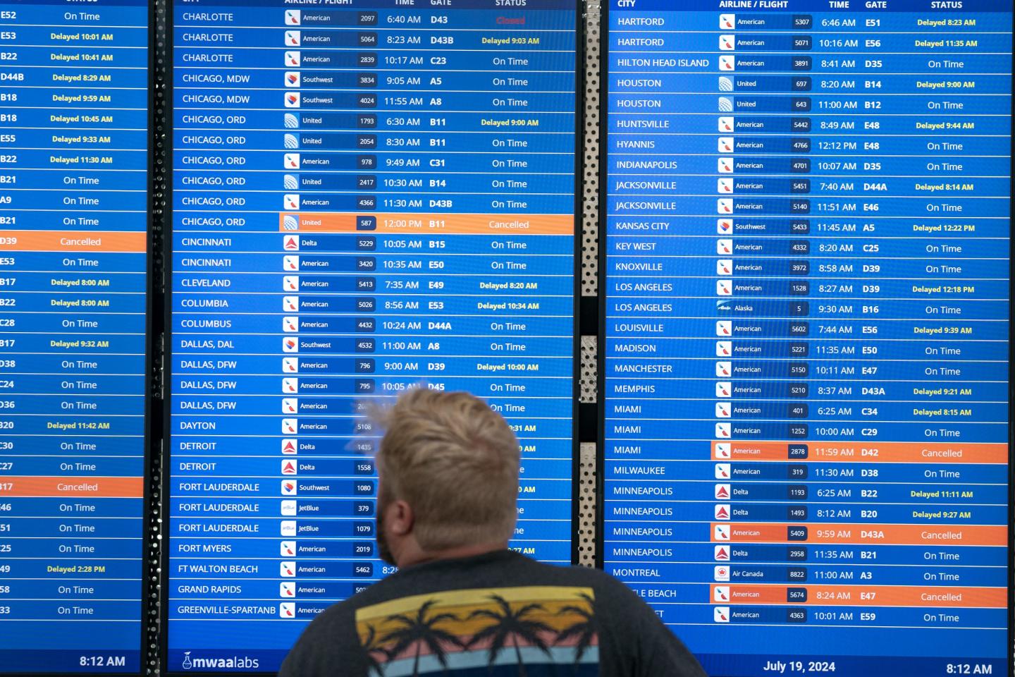 A man looks at an airport's board of delayed flights after the CrowdStrike outage