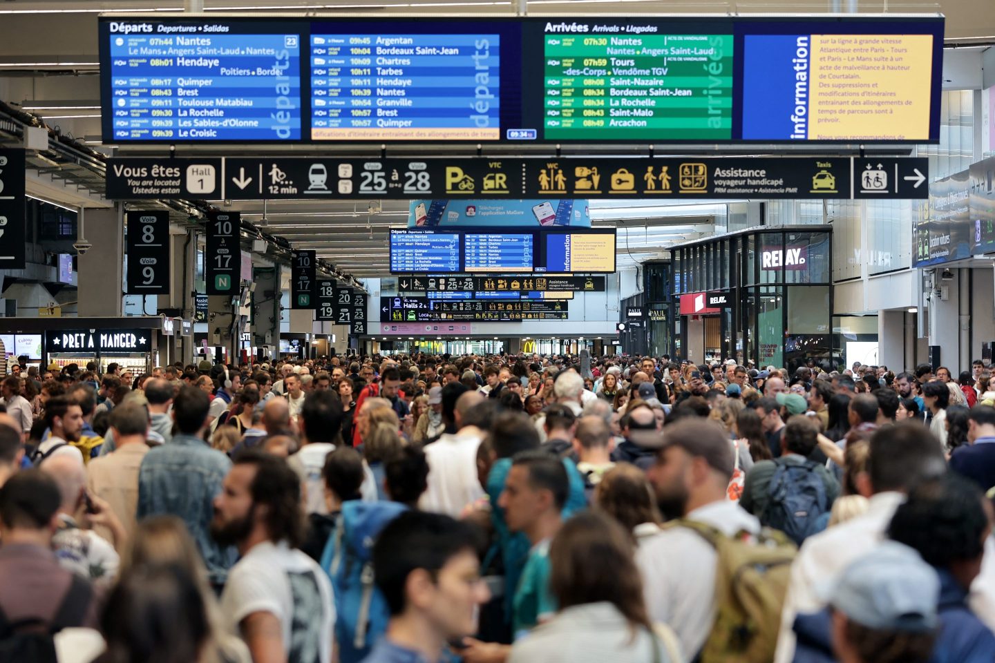 TOPSHOT - Passengers gather around the departure and arrival boards at the Gare Montparnasse train station in Paris on July 26, 2024 as France's high-speed rail network was hit by malicious acts disrupting the transport system hours before the opening ceremony of the Paris 2024 Olympic Games. According to SNCF a massive attack on a large scale hit the TGV network and many routes will have to be cancelled. SNCF urged passengers to postpone their trips and stay away from train stations. (Photo by Thibaud MORITZ / AFP) (Photo by THIBAUD MORITZ/AFP via Getty Images)