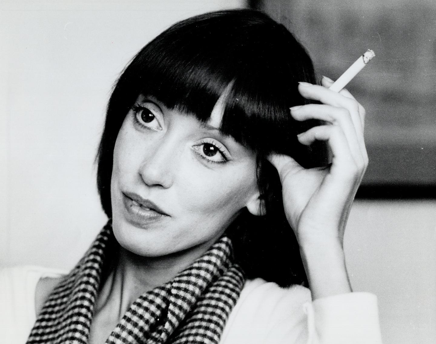 A black-and-white closeup of Shelley Duvall, holding a cigarette
