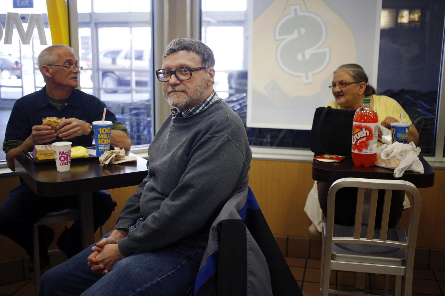 A man with gray hair sits in a McDonalds and looks at the camera.