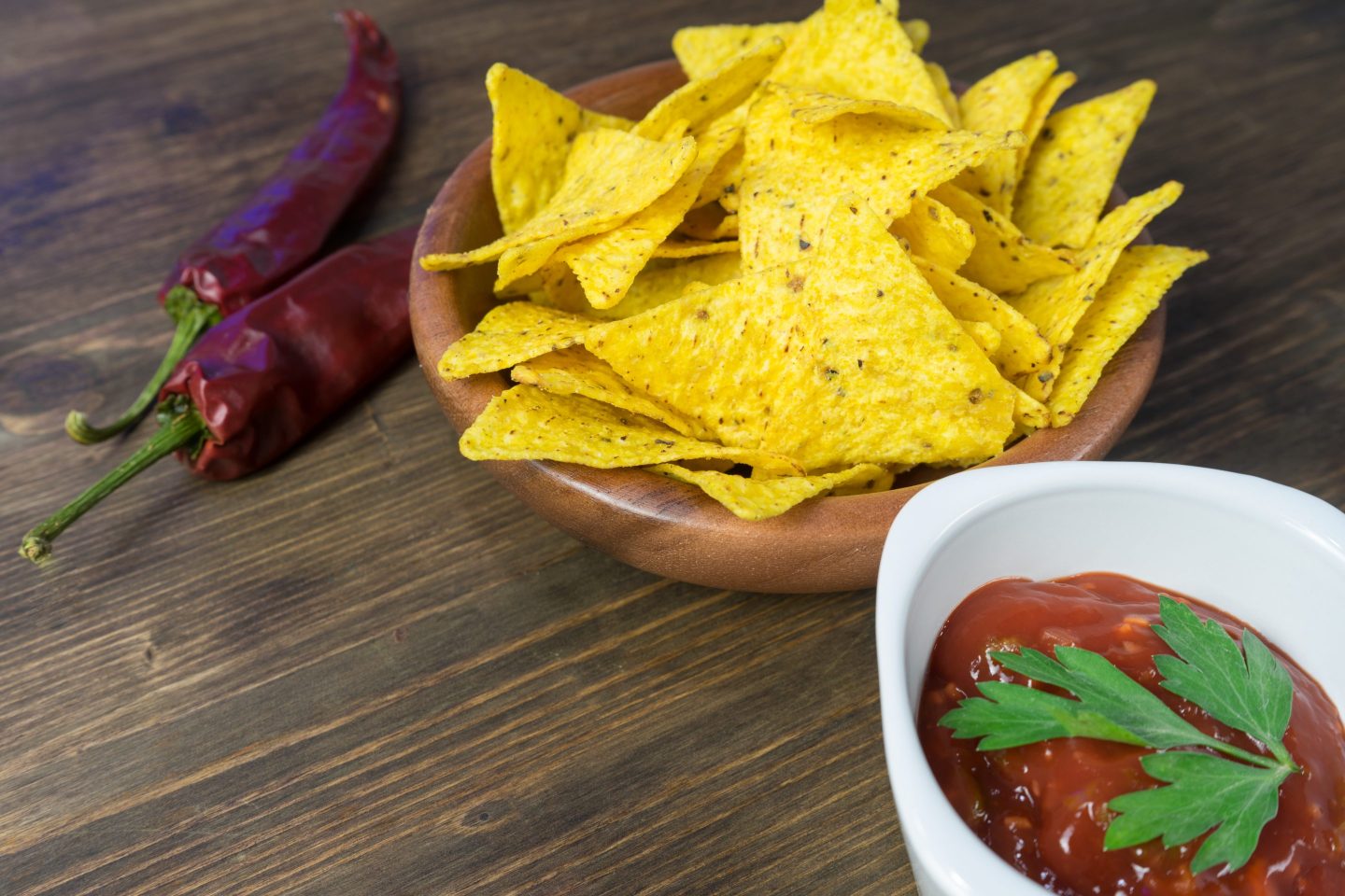A bowl of chips seen next to two peppers and salsa.