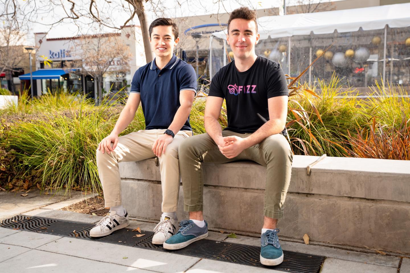 Two young men sit next to each other on a concrete bench.