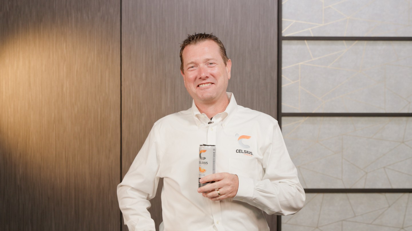 man in white shirt holding a can of Celsius energy drink