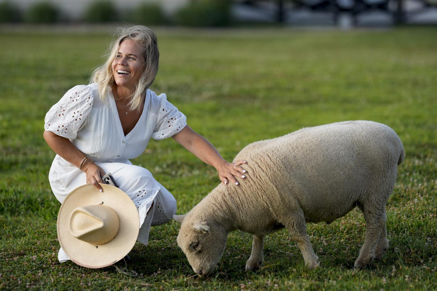 A woman smiles petting a tiny sheep