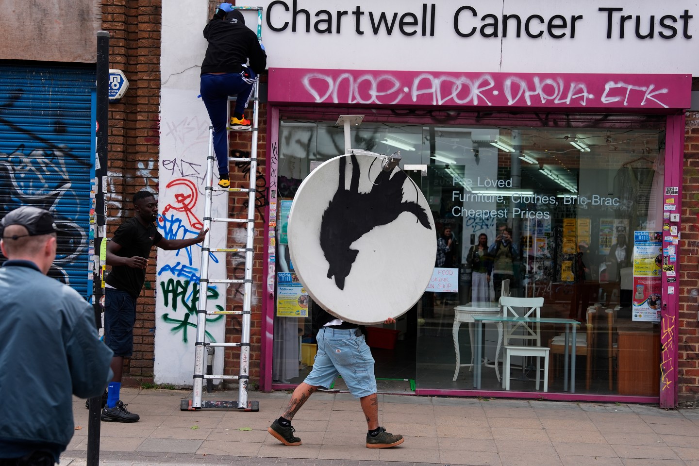 People remove a new artwork by Banksy, depicting a howling wolf painted on a satellite dish that was placed on a shop roof in Peckham, south London.