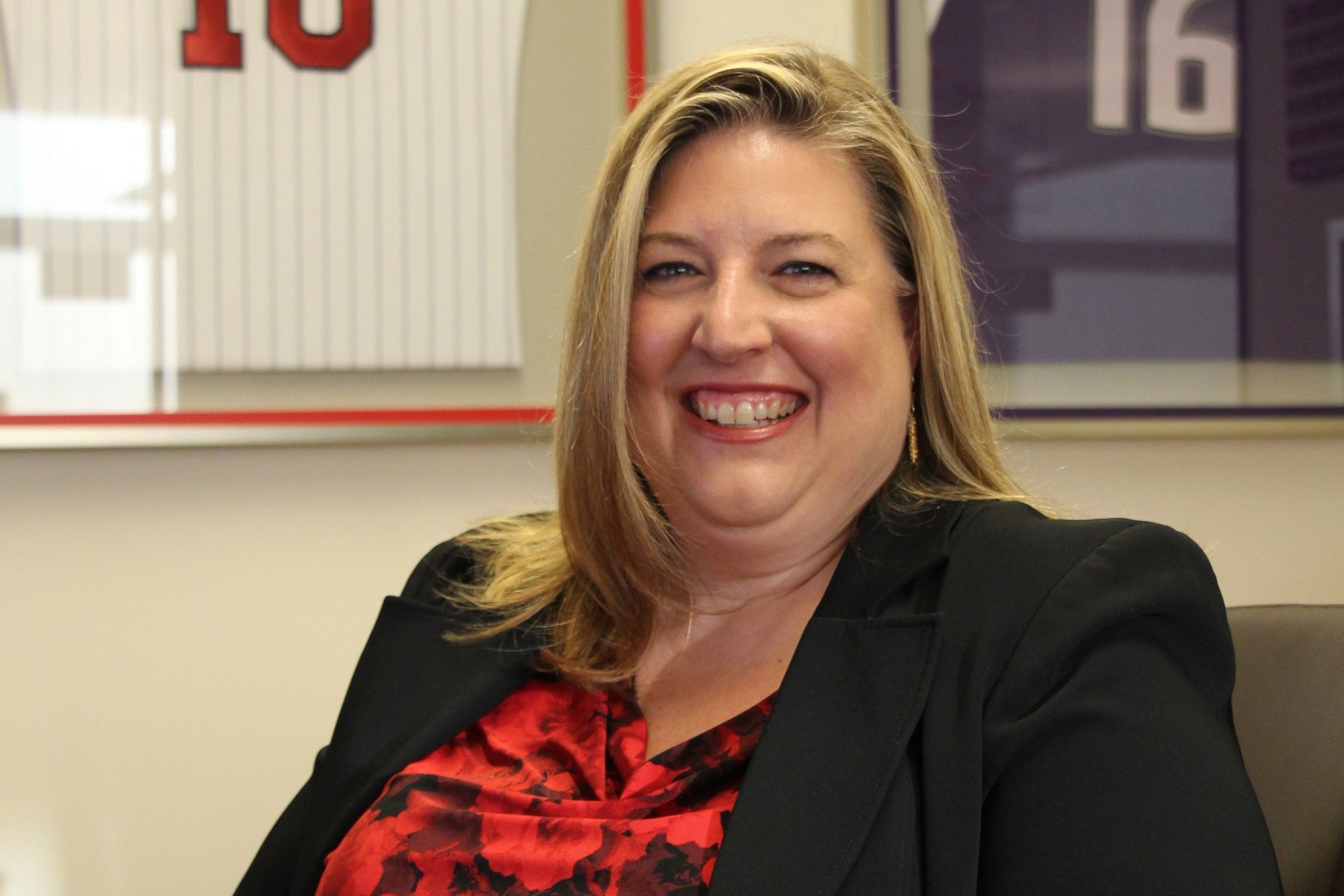 Stacy Sonnenberg, Goldman's global head of sports financing, sits smling in her office, in front of sports jerseys with her name on them.