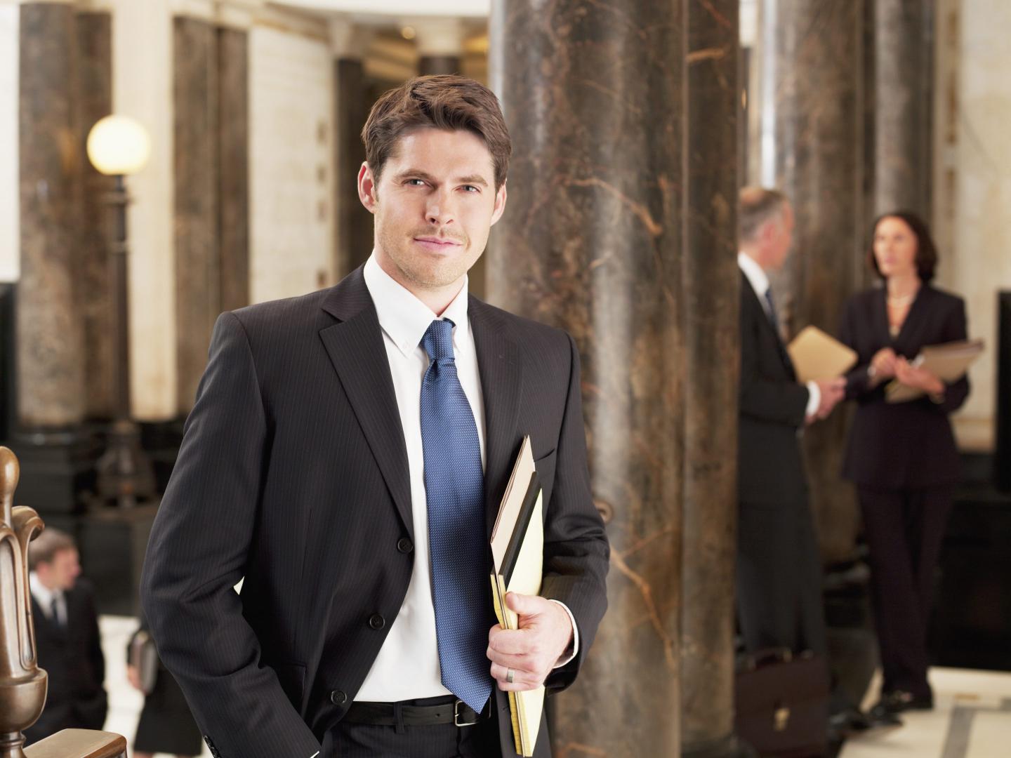 Smiling businessman leaning against pillar in corridor.