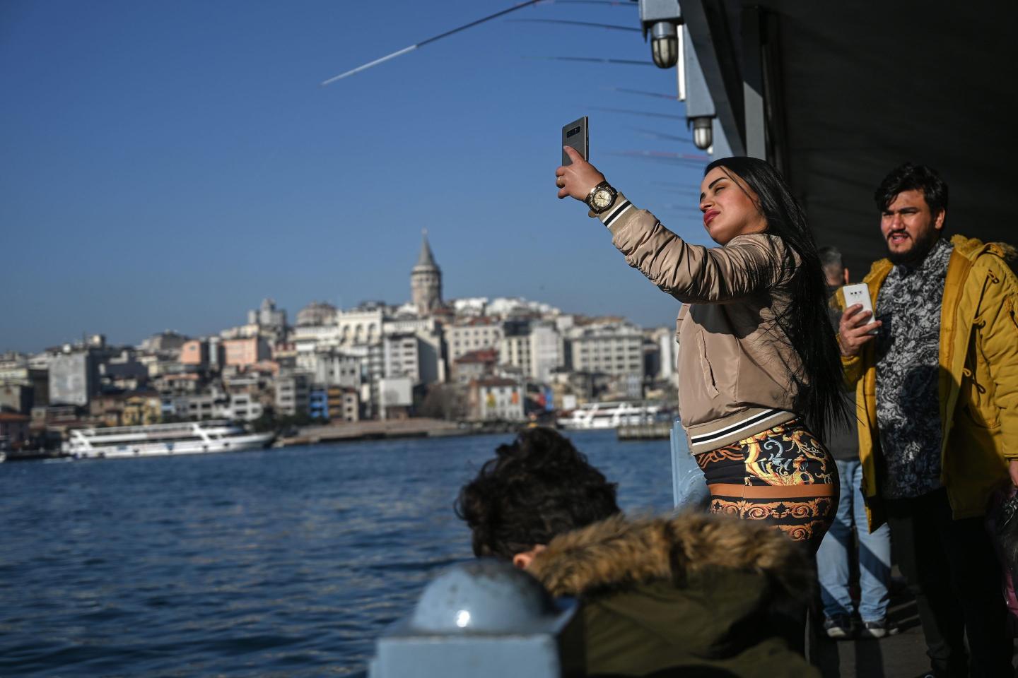 A woman uses her phone to take a selfie on the Galata bridge in Istanbul.